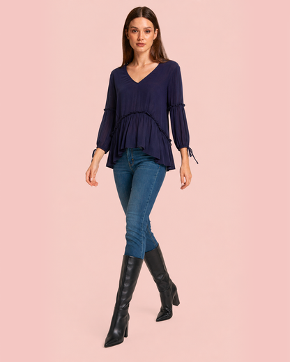 Woman wearing a navy blue top, jeans, and black knee-high boots on a pink background