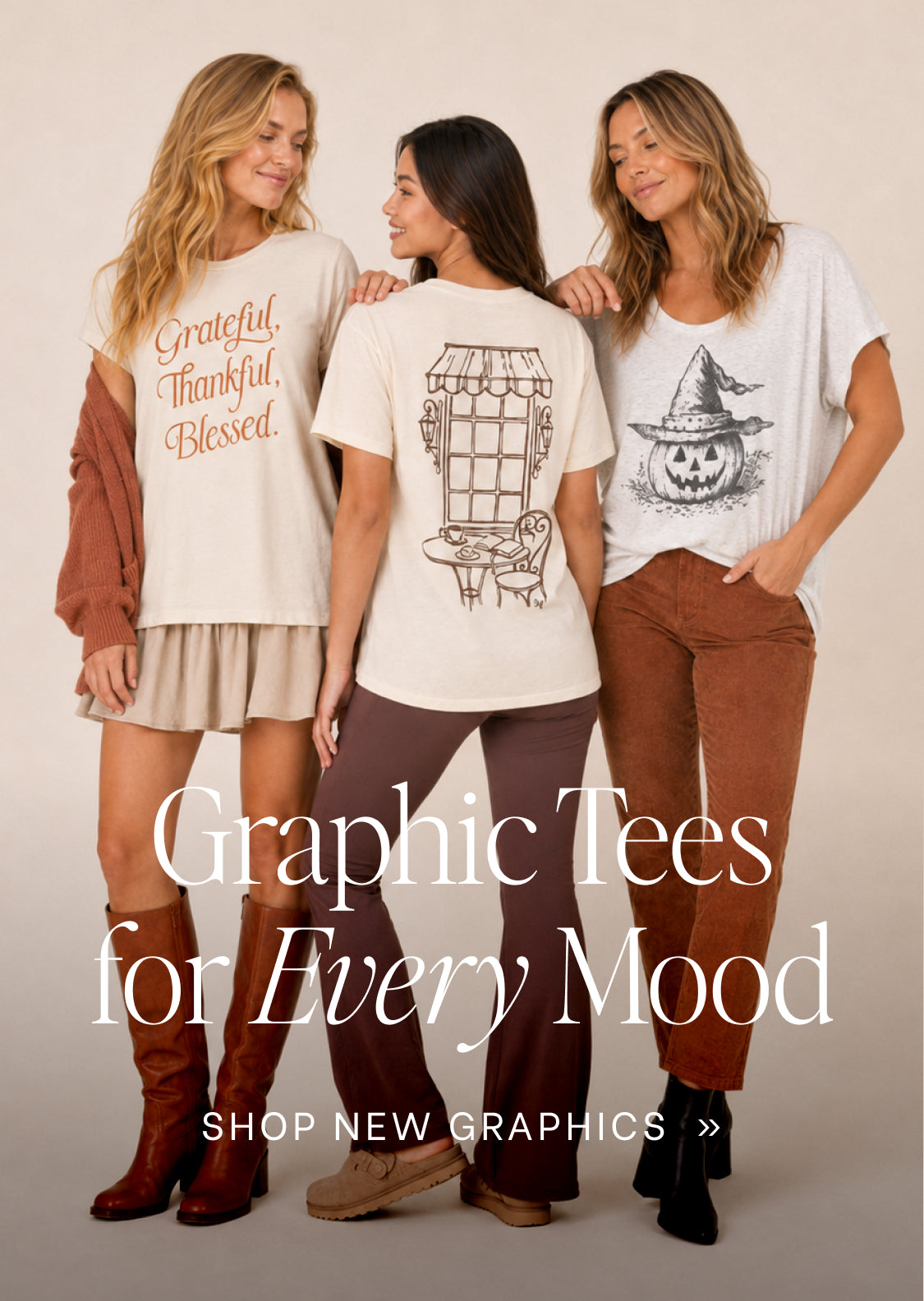 Three women modeling graphic t-shirts in a studio setting. The woman on the left wears a cream t-shirt with 'Grateful, Thankful, Blessed' in orange script.