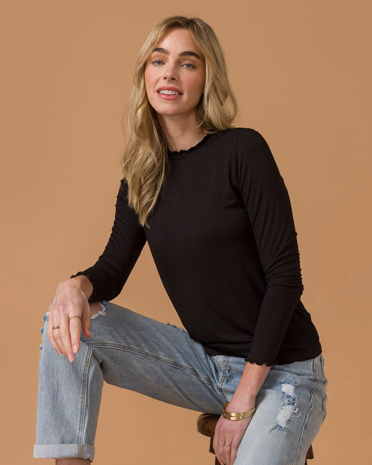 Woman wearing a black long-sleeve top and light blue jeans against a brown background