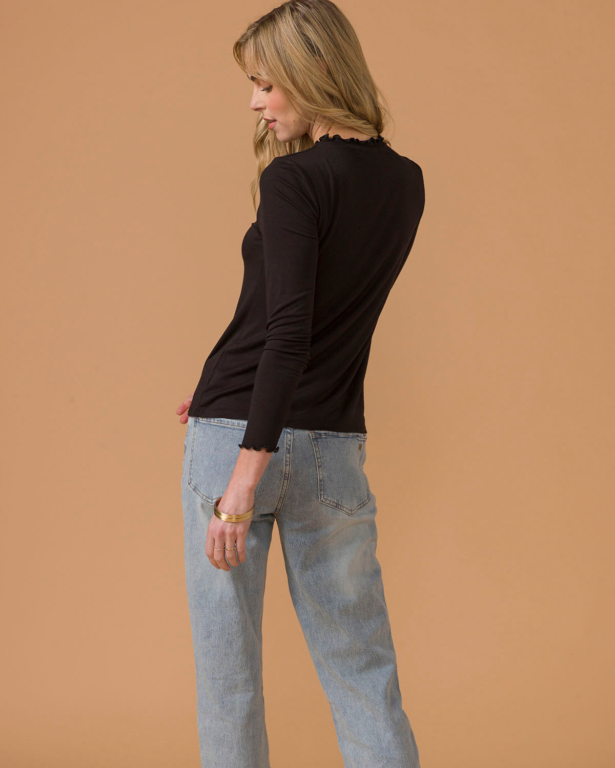 Woman wearing a black long-sleeve top and light blue jeans back view