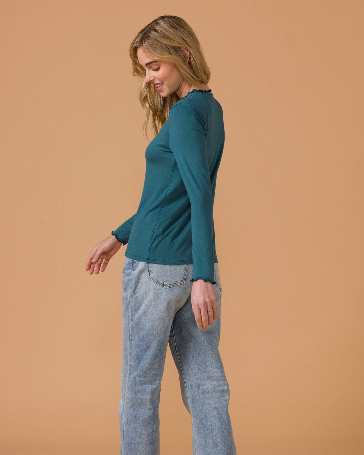 Woman wearing a teal long-sleeve top and light blue jeans side view
