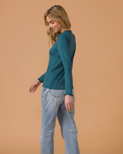 Woman wearing a teal long-sleeve top and light blue jeans side view