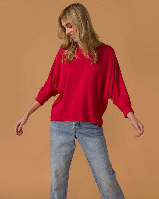 Seated woman wearing a red long sleeve top and blue jeans on a beige background