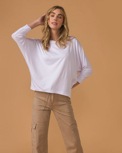 Woman wearing a white long sleeve top and beige pants against a brown background
