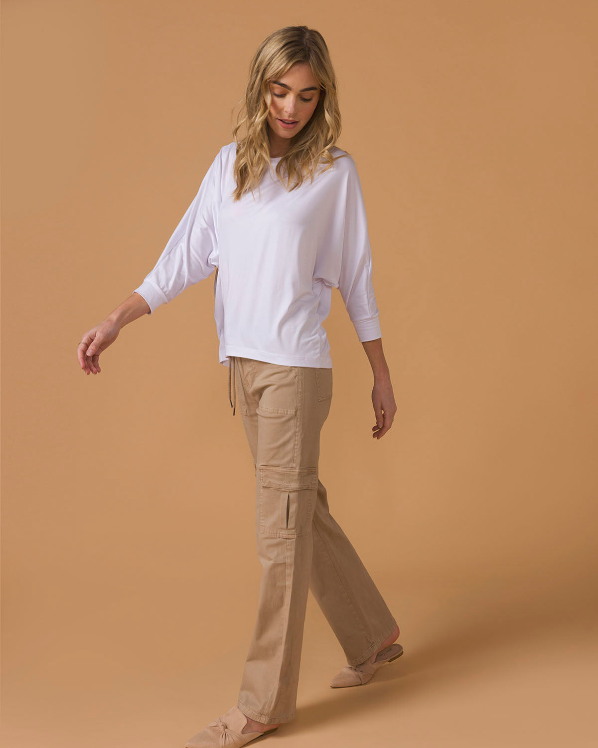 Side view of a woman wearing a white long sleeve top and beige pants 