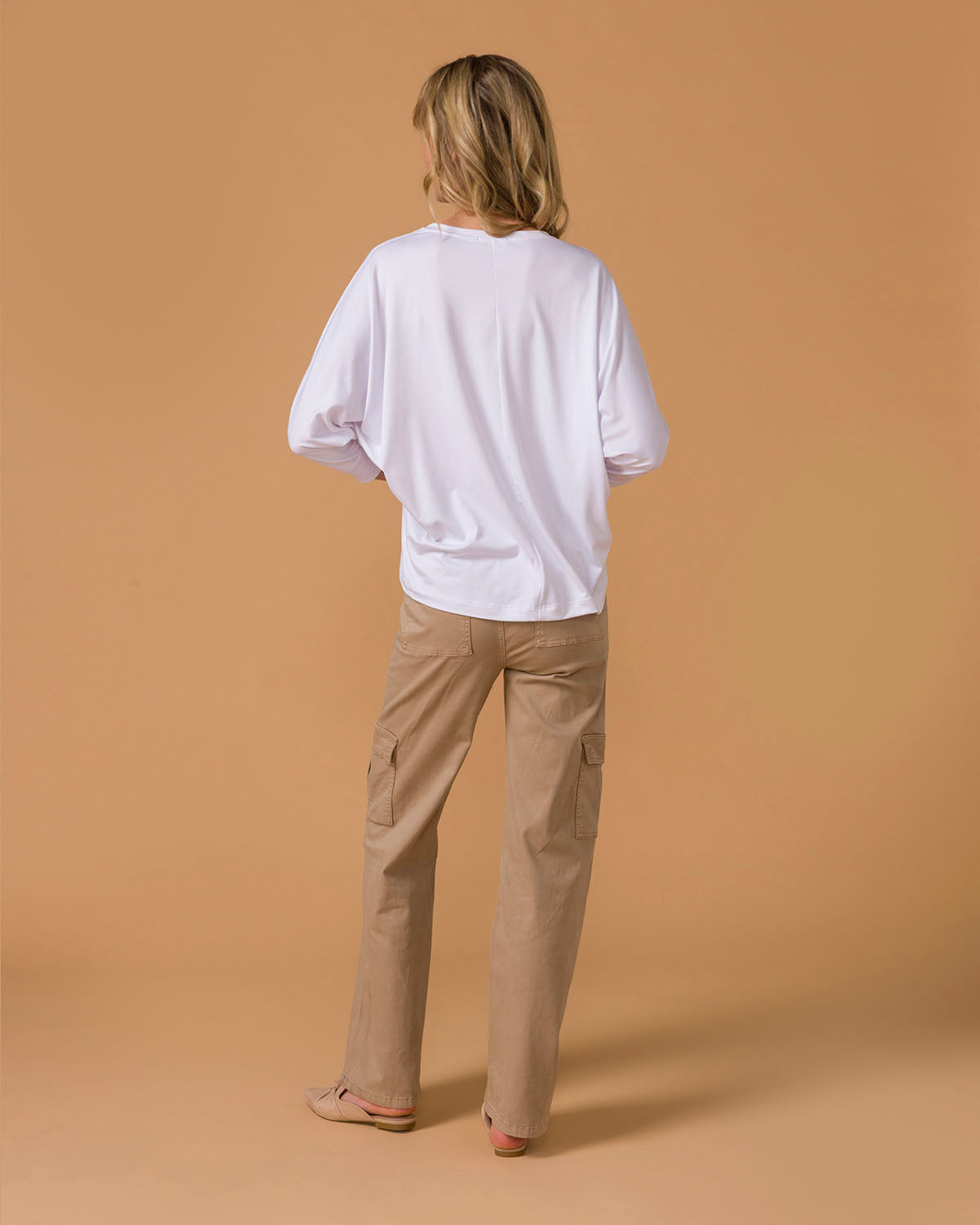 Woman wearing a white long-sleeve top and beige pants back view