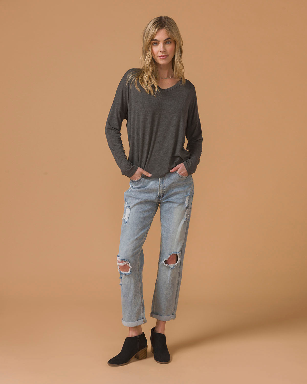 Woman wearing a dark gray long sleeve top and light blue jeans on a beige background