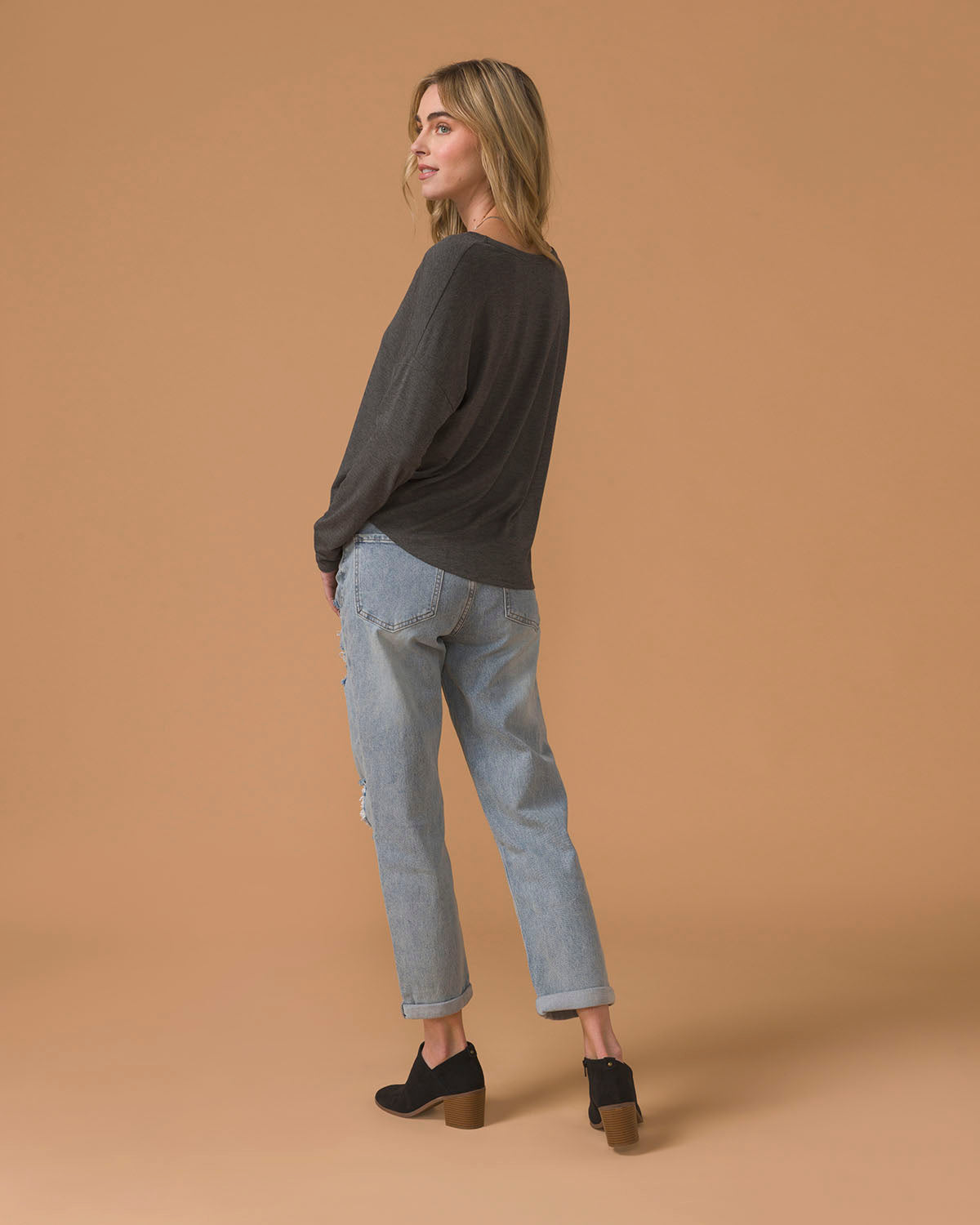 Woman wearing a dark gray sweater and light blue jeans, back view, on a beige background