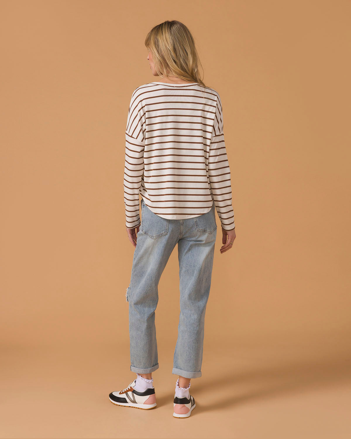 Person wearing a striped long sleeve top and jeans on a beige background, back view