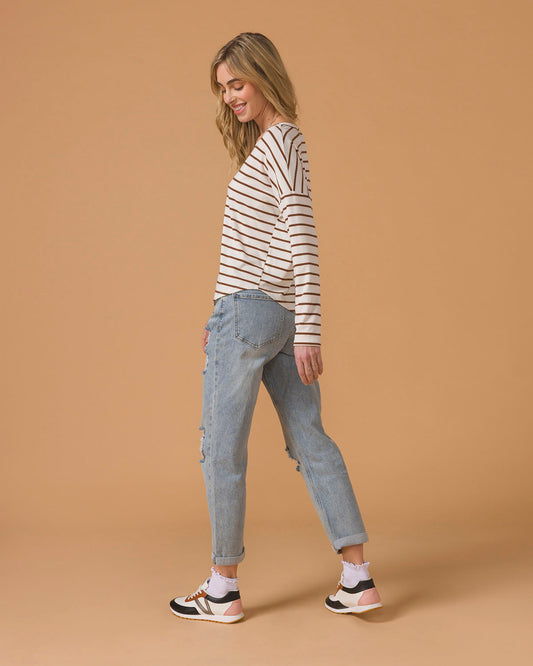Woman wearing a striped long sleeve top and blue jeans sitting on a stool on a beige background