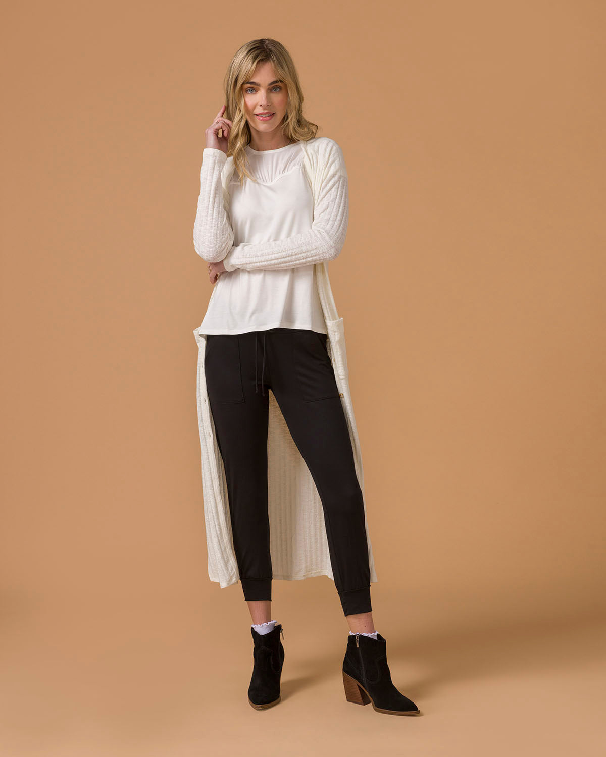 Long cream cardigan worn by a woman with white top and black pants, beige background