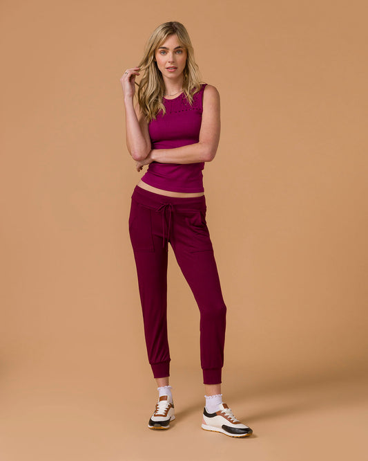 Woman wearing a deep purple tank top and maroon pants on a beige background