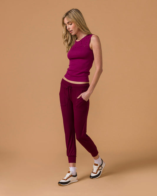 Woman wearing a deep purple tank top and maroon pants on a beige background