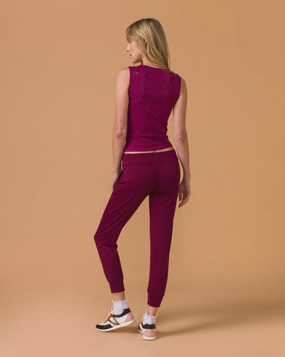 Woman wearing a deep purple tank top and maroon pants, back view