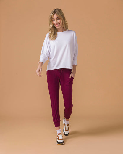 Woman wearing a white long sleeve top and maroon  jogger pants on a beige background
