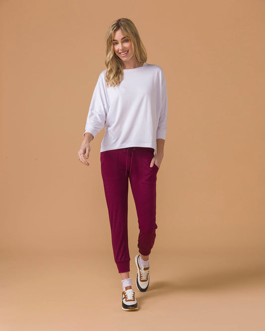 Woman wearing a white long sleeve top and maroon  jogger pants on a beige background