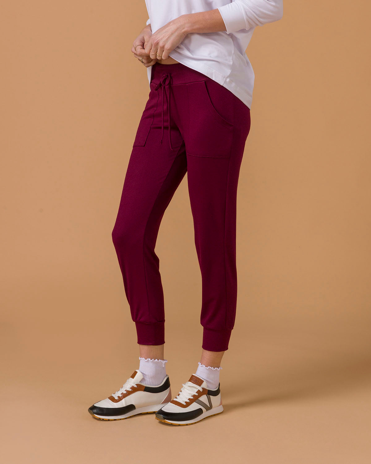 Side view of a woman wearing maroon jogger pants, lower half visible, on a beige background