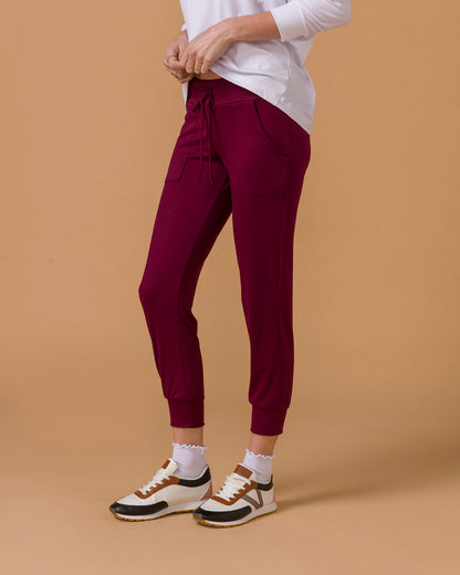 Side view of a woman wearing maroon jogger pants, lower half visible, on a beige background