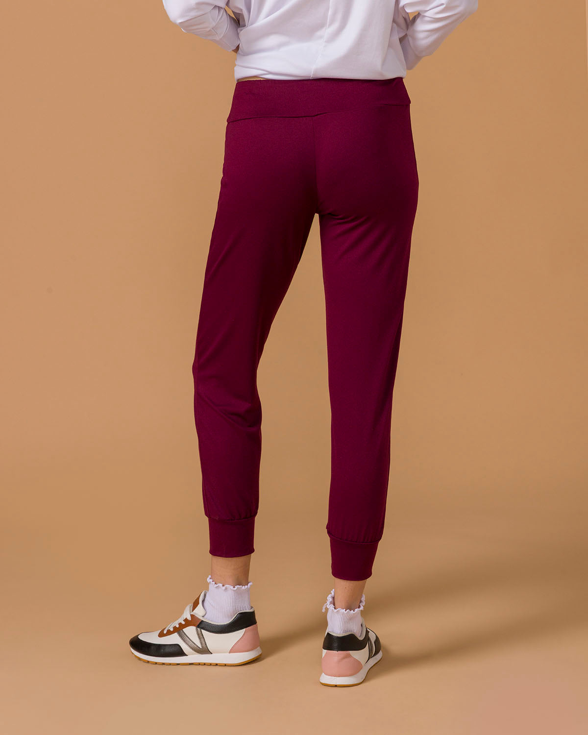 Person wearing maroon jogger pants on a beige background, back view