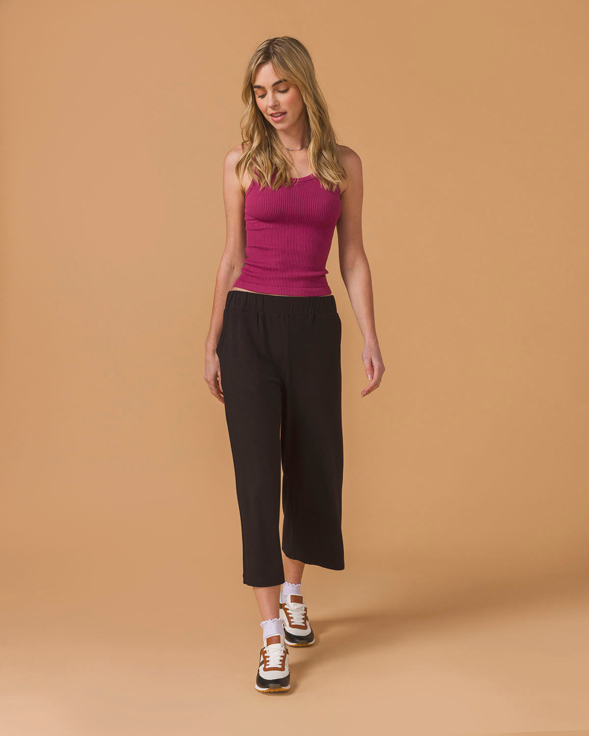 Woman wearing a purple top and a black wide leg crop pants on a beige background