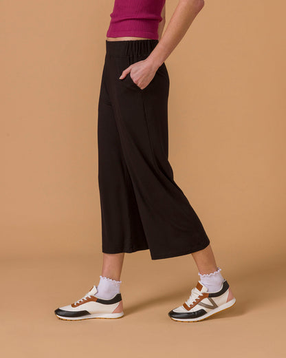 Side view of a woman wearing black wide leg pants, lower half visible, on a beige background