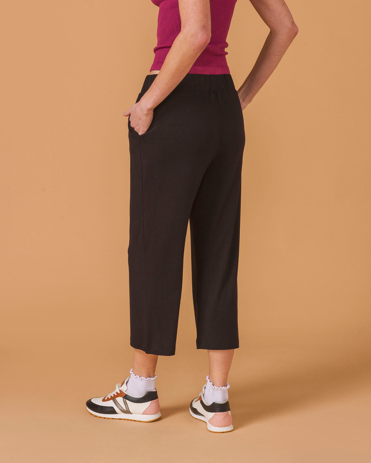 Back view of a person wearing black wide leg pants on a brown background