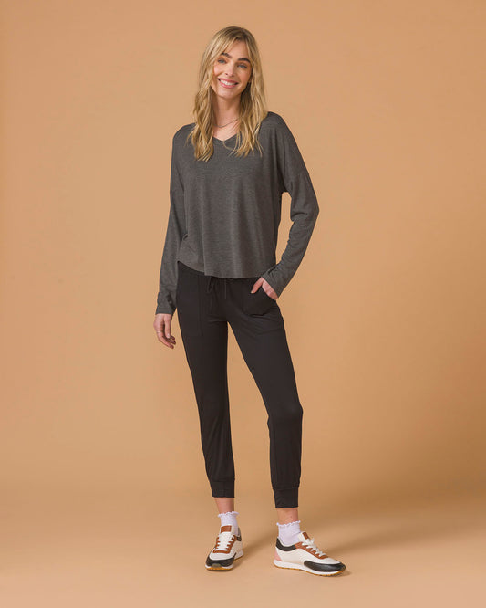 Woman sitting on a beige floor wearing a gray long sleeve top and black pants