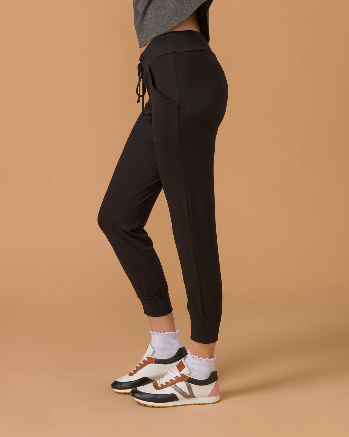 Side view of a woman wearing black pants, lower half visible, on a beige background