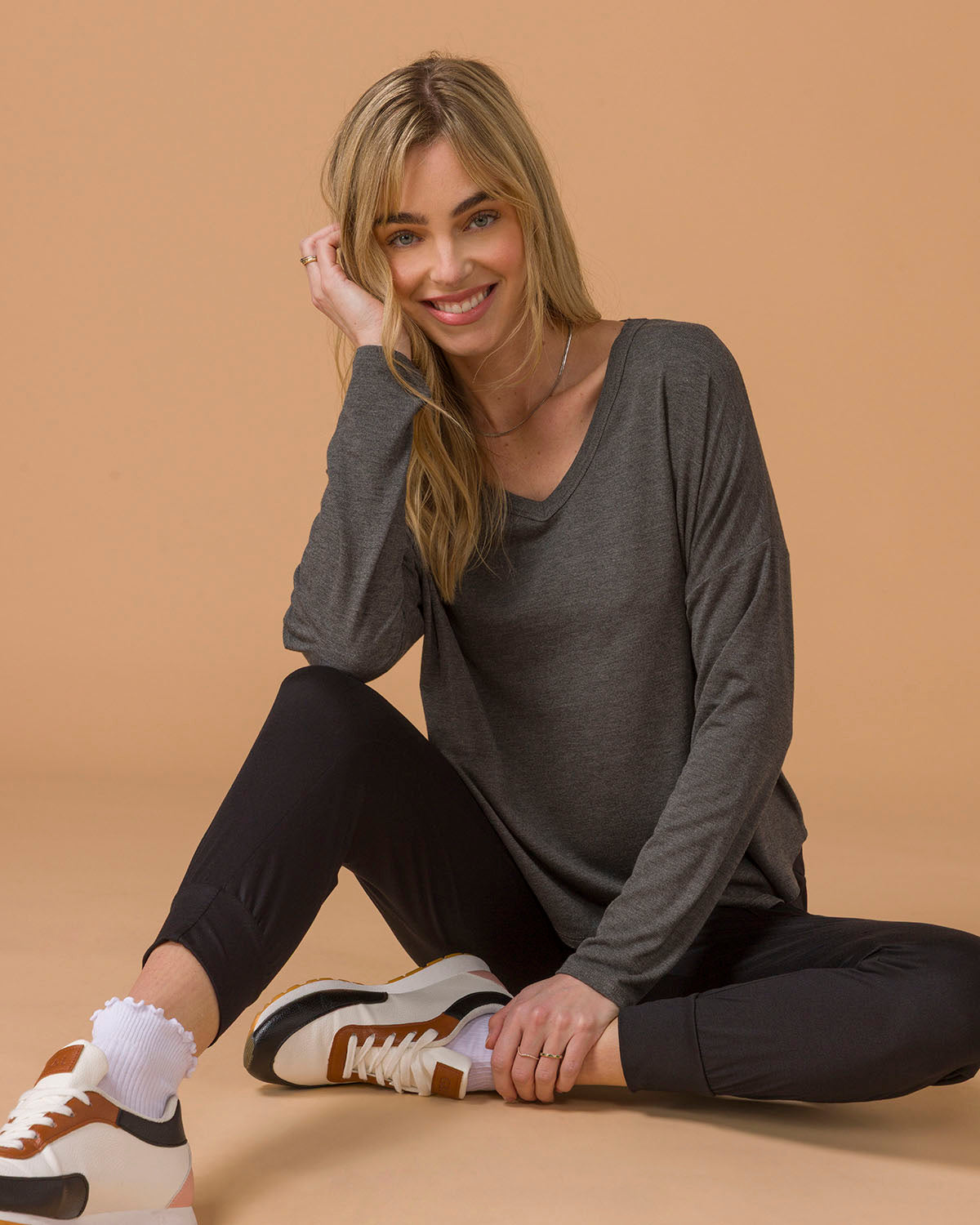 Woman sitting on a beige floor wearing a gray long sleeve top and black pants