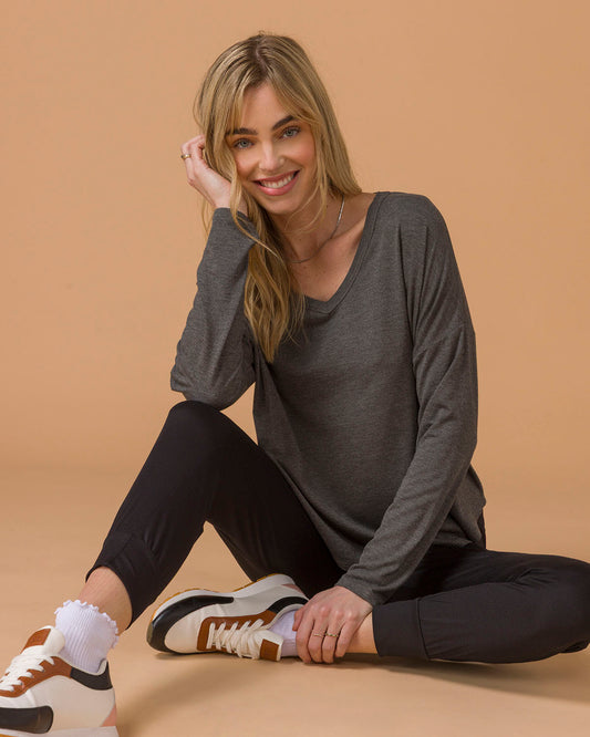 Woman sitting on a beige floor wearing a gray long sleeve top and black pants