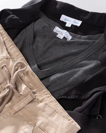 Flat lay of a dark gray v-neck shirt layered under a black jacket next to beige pants