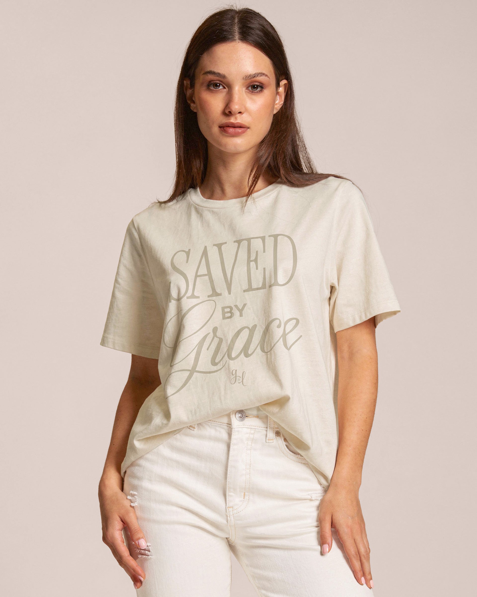 Woman wearing a cream t-shirt with 'Saved by Grace' text on a plain background