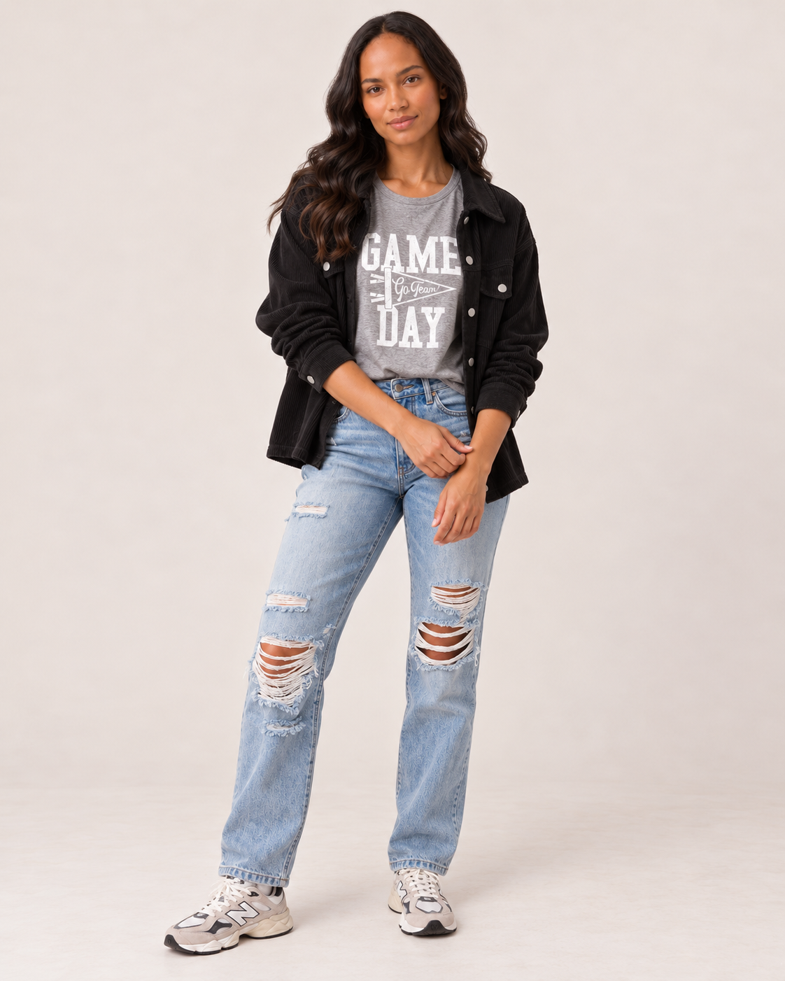 A woman modeling a black button-up jacket over a gray graphic t-shirt, paired with light-wash distressed blue jeans and white sneakers, against a plain light beige studio background.