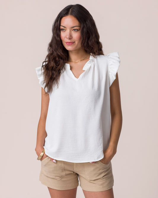 Woman wearing a white blouse with ruffled shoulders and beige shorts on a plain background