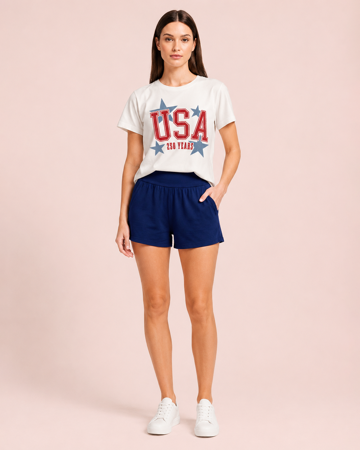 Front view of a woman wearing a white USA graphic tee and navy lounge shorts on a beige background