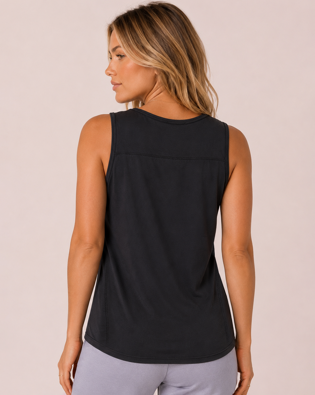 Back view of a woman wearing a black tank top with lavender pants on a beige background