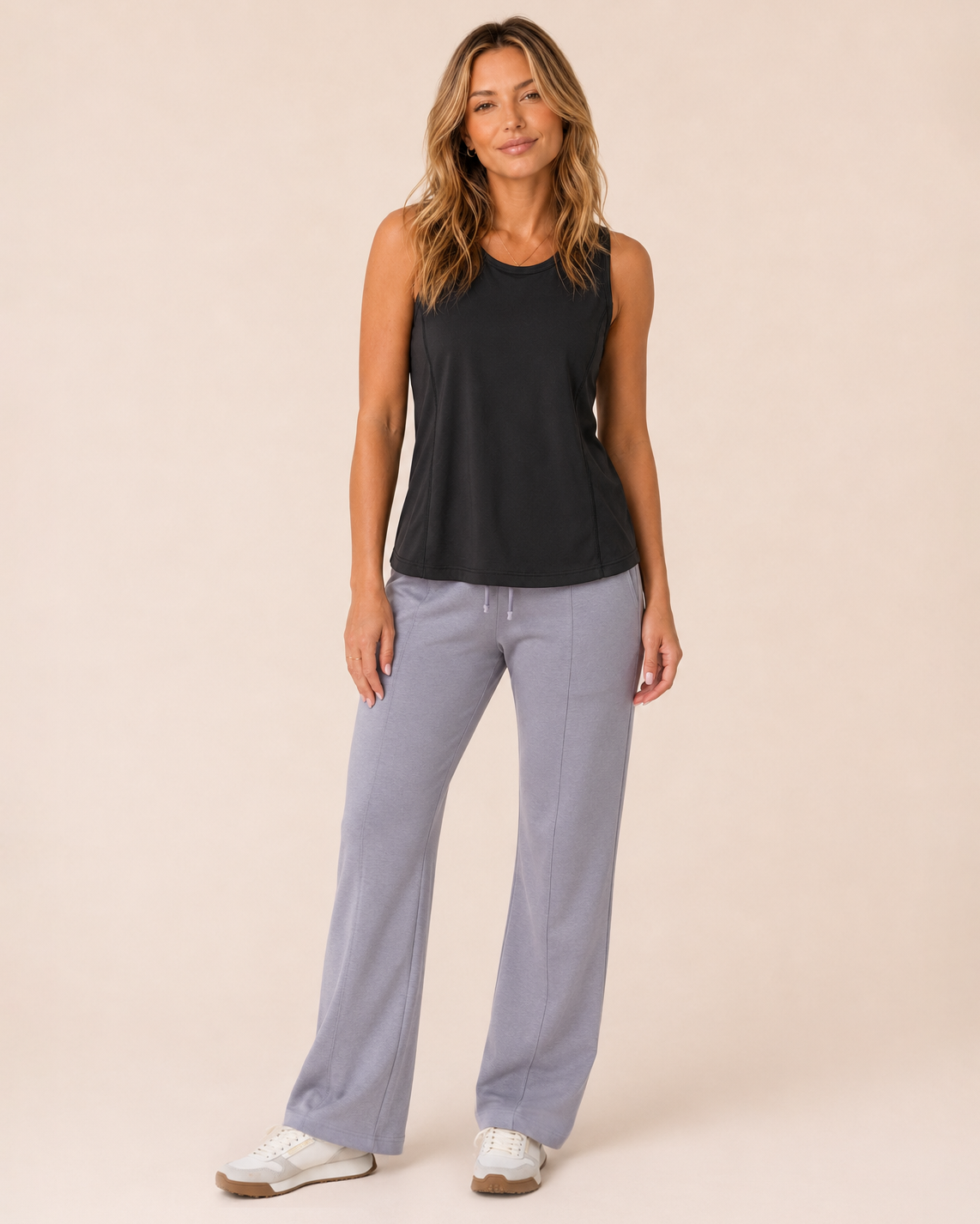 Back view of a woman wearing a black tank top with lavender pants on a beige background