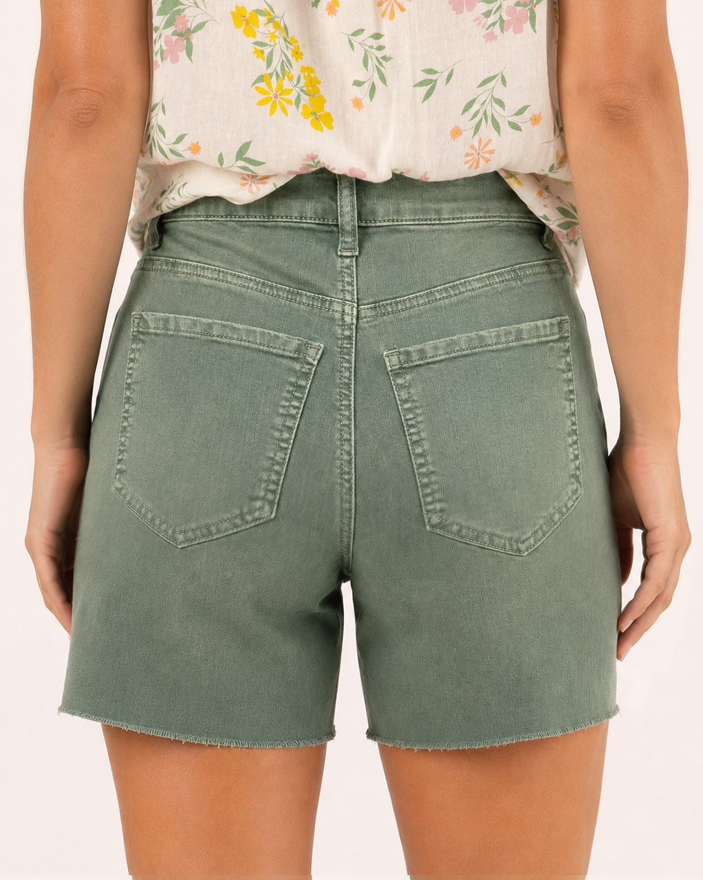 Back view of a woman wearing sage distressed shorts and a floral sleeveless blouse on a beige background