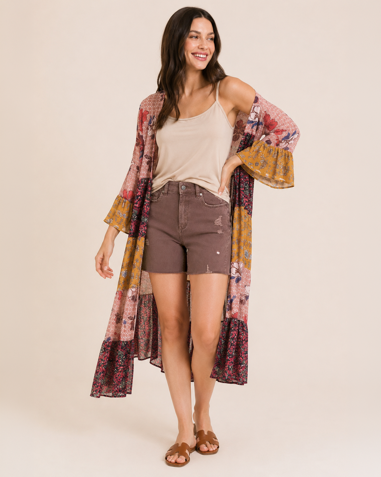 Front view of a woman wearing wine distressed shorts, a beige sleeveless top, and a multicolored plaid shirt on a beige background