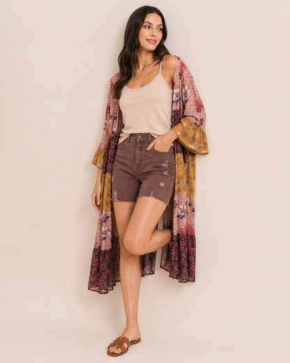 Full-body view of a woman wearing wine distressed shorts, a beige sleeveless top, a multicolored plaid shirt, and brown sandals on a beige background