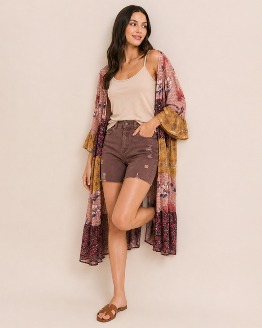 Full-body view of a woman wearing wine distressed shorts, a beige sleeveless top, a multicolored plaid shirt, and brown sandals on a beige background