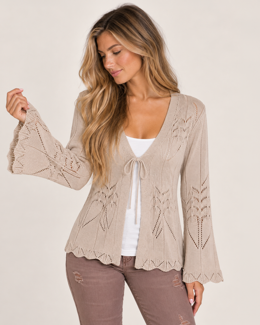 Cropped front view of a woman wearing a taupe open-front knit cardigan with lace-patterned sleeves over a white top on a beige background