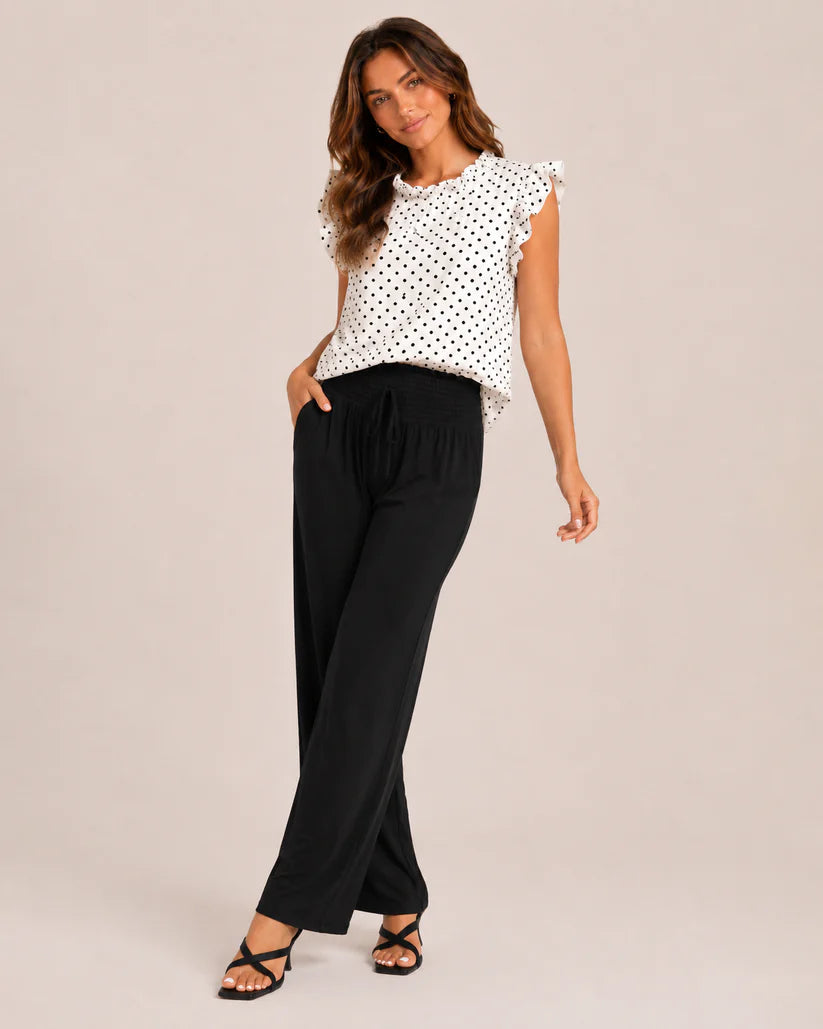 Woman wearing a ruffle sleeve polka dot top and black pants on a beige background