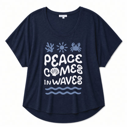 Navy graphic tee featuring a "Peace Comes in Waves" design on a beige background
