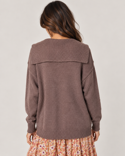 Back view of a woman wearing a mauve long-sleeve knit cardigan with a floral pleated midi skirt on a beige background.