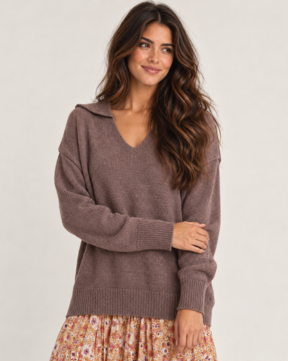 Cropped front view of a woman wearing a mauve V-neck knit cardigan with long sleeves, paired with a floral pleated skirt on a beige background.