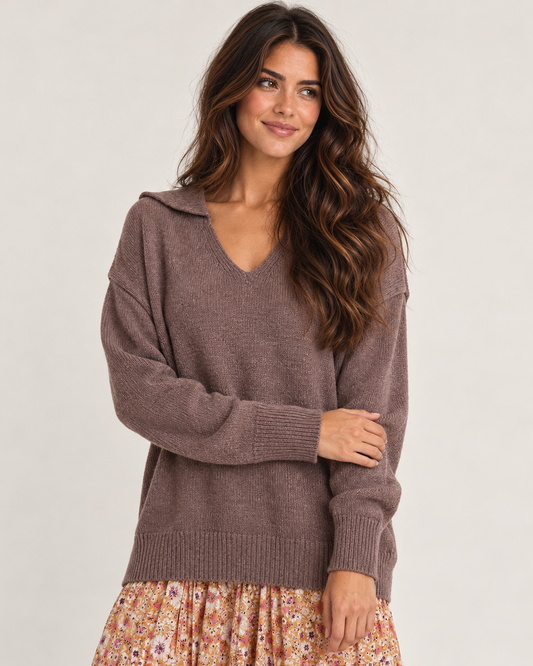 Cropped front view of a woman wearing a mauve V-neck knit cardigan with long sleeves, paired with a floral pleated skirt on a beige background.