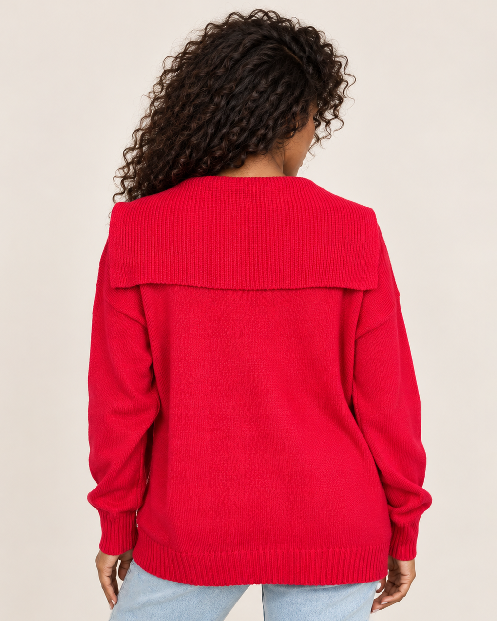Back view of a woman wearing a bright red long-sleeve pullover with light-wash jeans, showing the relaxed fit and back design on a beige background.