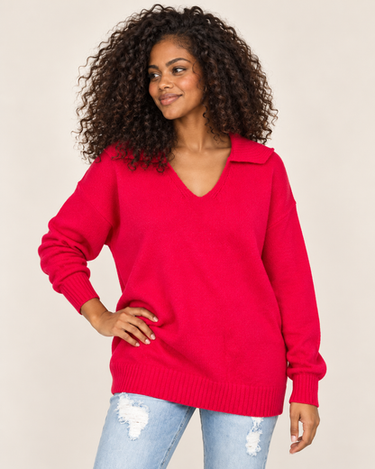Cropped front view of a woman wearing a bright red long-sleeve pullover with ribbed cuffs and light-wash distressed jeans on a beige background.