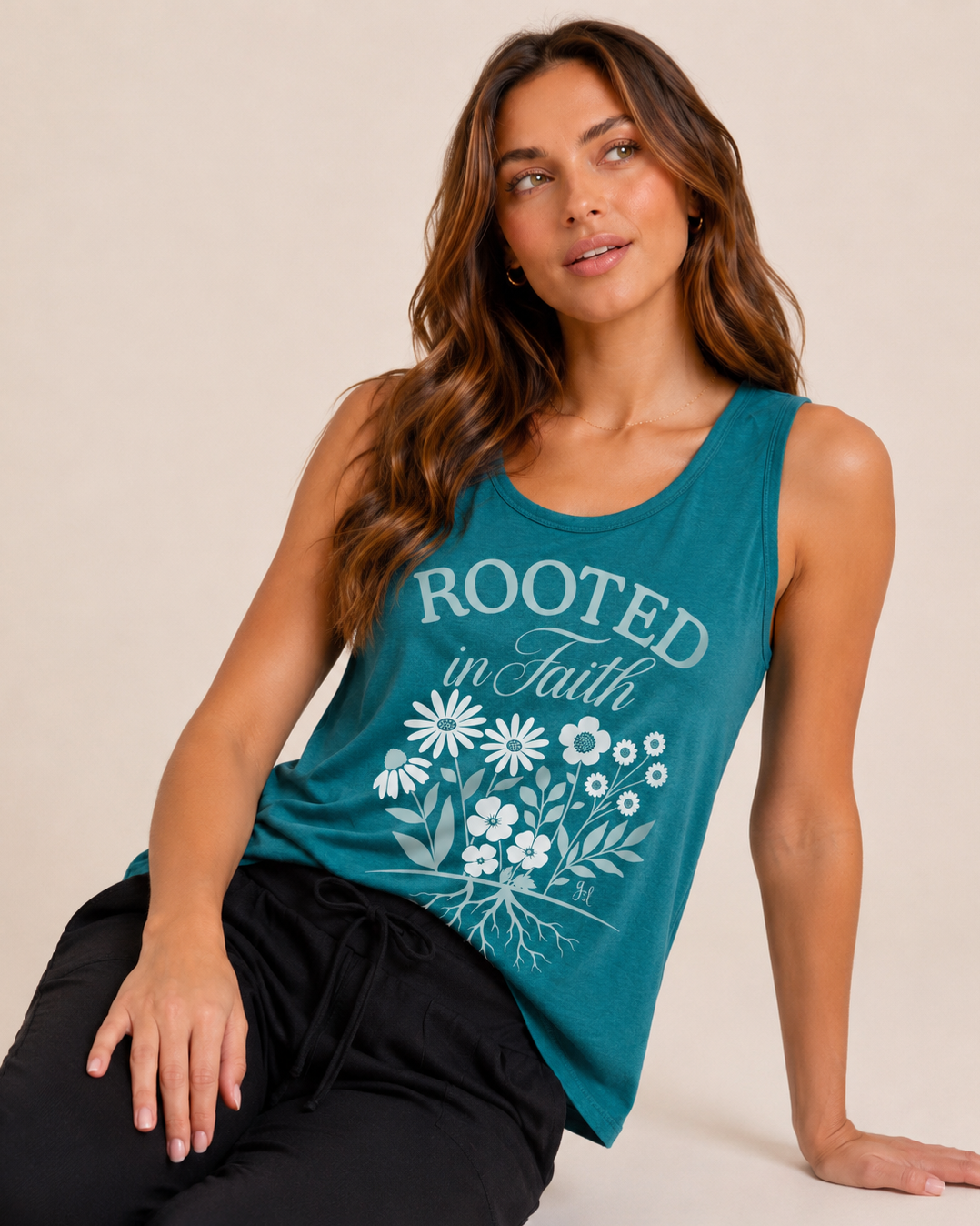 Close-up of a woman wearing a teal graphic tank top featuring a "Rooted in Faith" floral design and black jogger pants on a beige background